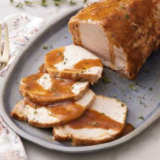 A platter of Instant Pot pork loin garnished with fresh thyme. A fork on the side.
