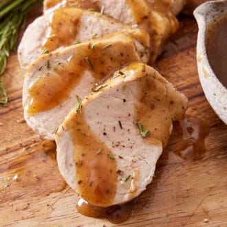 A close up view of sliced Instant Pot pork tenderloin with gravy on top. A bowl of gravy on the side with pepper and rosemary.