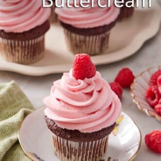 Pinterest graphic of a plate with a cupcake topped with raspberry buttercream frosting and a fresh raspberry. More frosted cupcakes in the background.