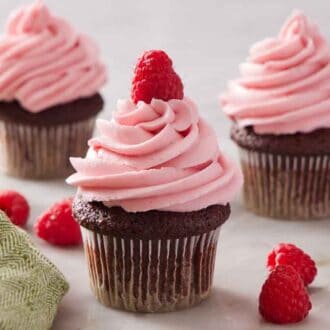 Three cupcakes topped with raspberry buttercream with one in the center topped with a raspberry.