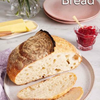 Pinterest graphic of a plate with a loaf of sourdough bread with two slices cut off in front. A jar of jam, plates, butter, flowers, and coffee in the background.