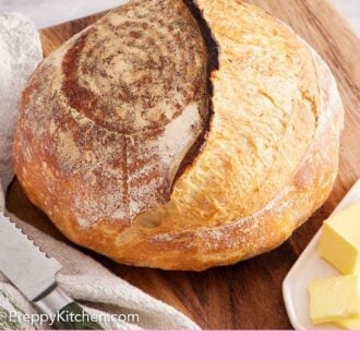 Pinterest graphic of a loaf of sourdough bread on a wooden serving board with some butter on the side.