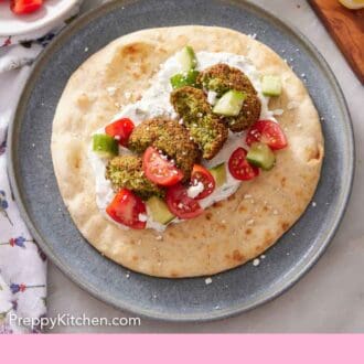 Pinterest graphic of pita bread on a plate with cut air fryer falafel with sauce, cut cucumbers, and tomatoes.