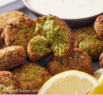 Pinterest graphic of a pile of air fryer falafel with one cut opened, showing the interior. Bowl of sauce in the back and some lemon wedges.
