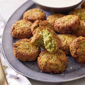 A platter of air fryer falafel with one cut opened, showing the interior. Lemon wedges on the side. A fork beside the platter.