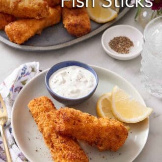 Pinterest graphic of a plate with two air fryer fish sticks with lemon wedges and a bowl of tartar sauce. A platter of more air fryer fish sticks in the background.