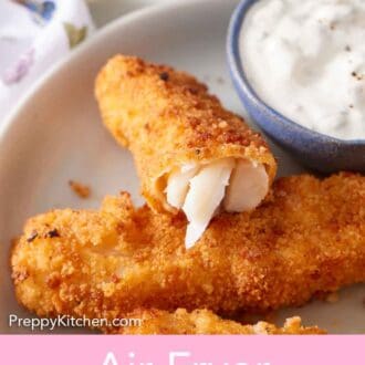Pinterest graphic of an air fryer fish stick cut opened, showing the fish inside, propped up on another fish stick with a bowl of tartar sauce beside it.