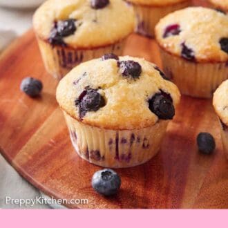 Pinterest graphic of blueberry muffins on a wooden serving board with fresh blueberries scattered around.