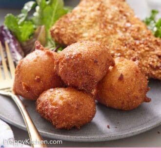 Pinterest graphic of a plate with four hush puppies with fried fish, mixed greens, and a fork.