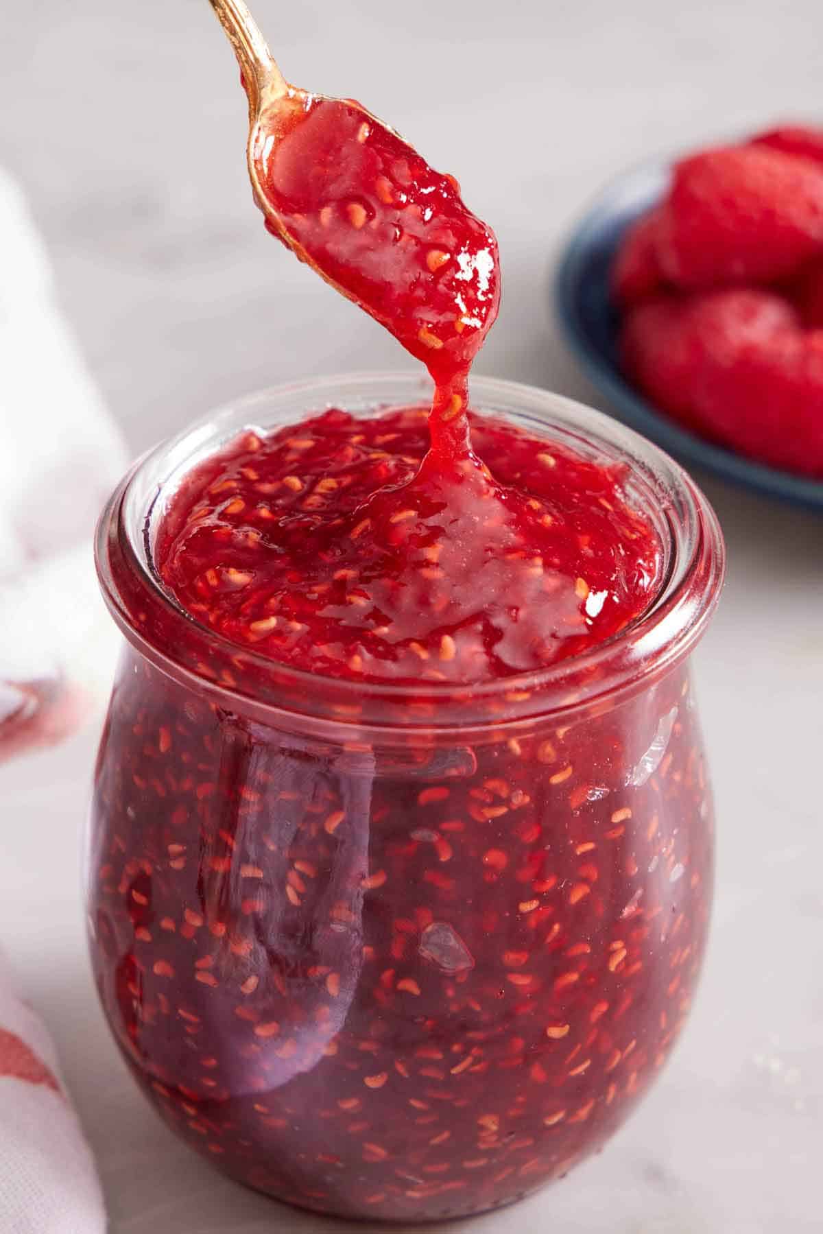 A spoon lifting up some raspberry jam from a jar.