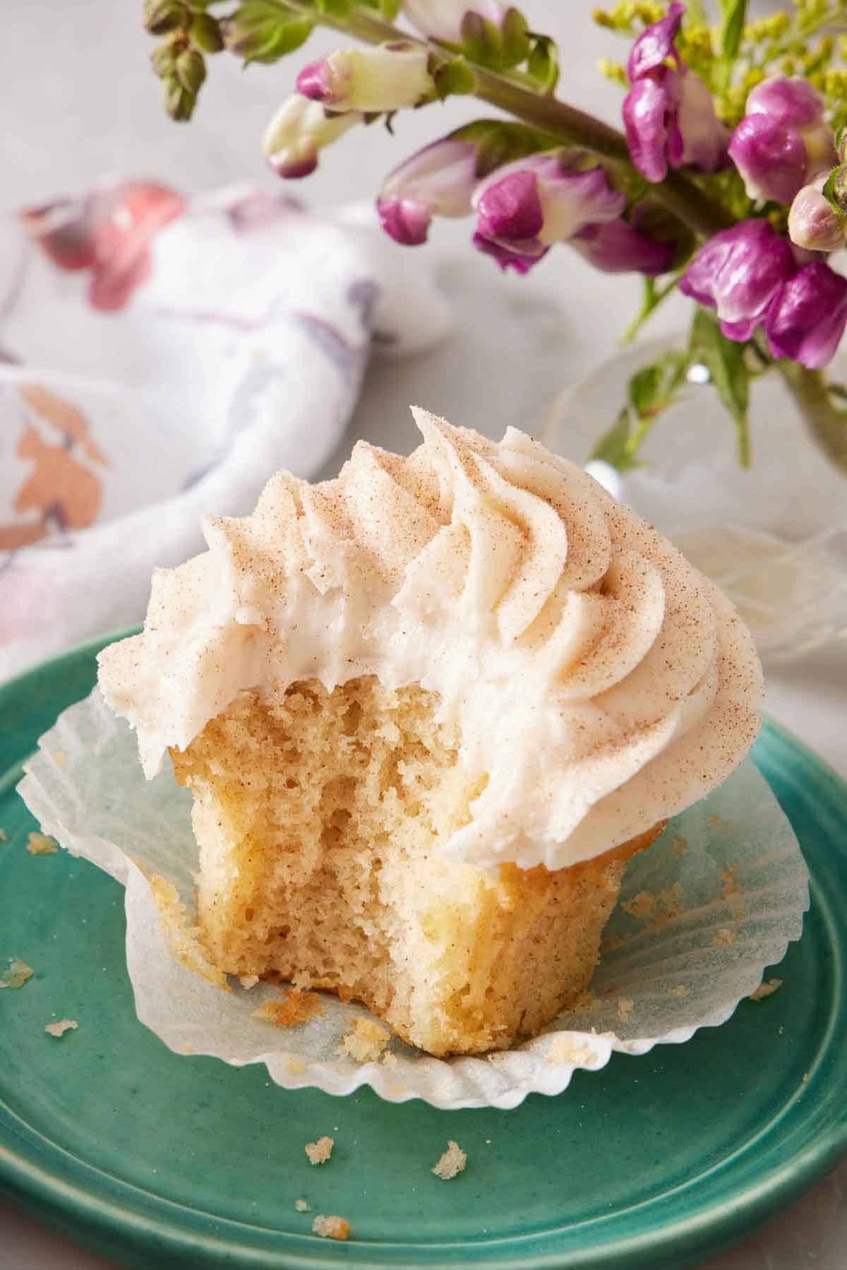 A plate with a snickerdoodle cupcake with the liner peeled down and a bite taken out of it.