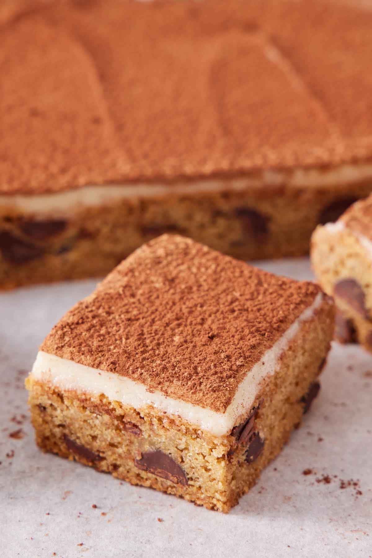 A piece of tiramisu blondie cut from the slab in the background.