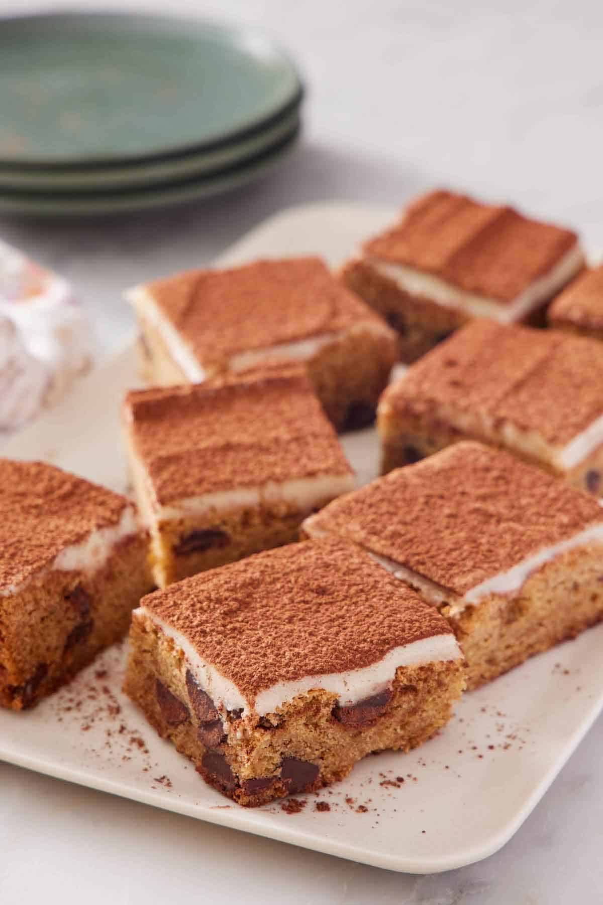 Multiple pieces of tiramisu blondies on a plate with a stack of three plates in the background.