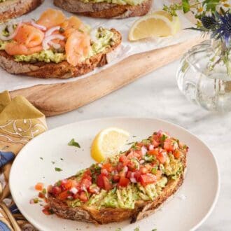 Pinterest graphic of a plate with avocado toast topped with pico de gallo and a lemon wedge on the side. A wooden serving board in the background with three pieces of avocado toast with various toppings and some flowers on the side.