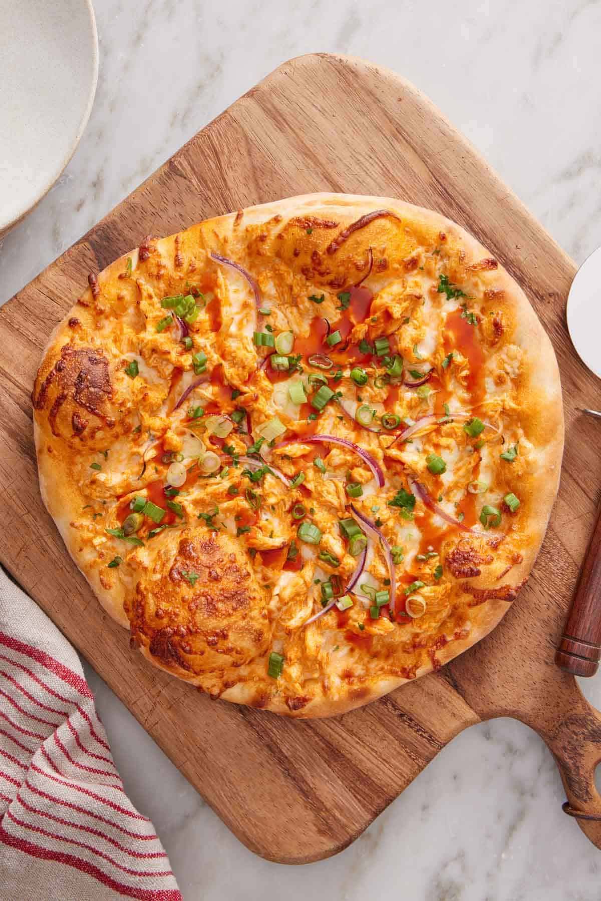 Overhead view of an uncut buffalo chicken pizza on a wooden serving board.