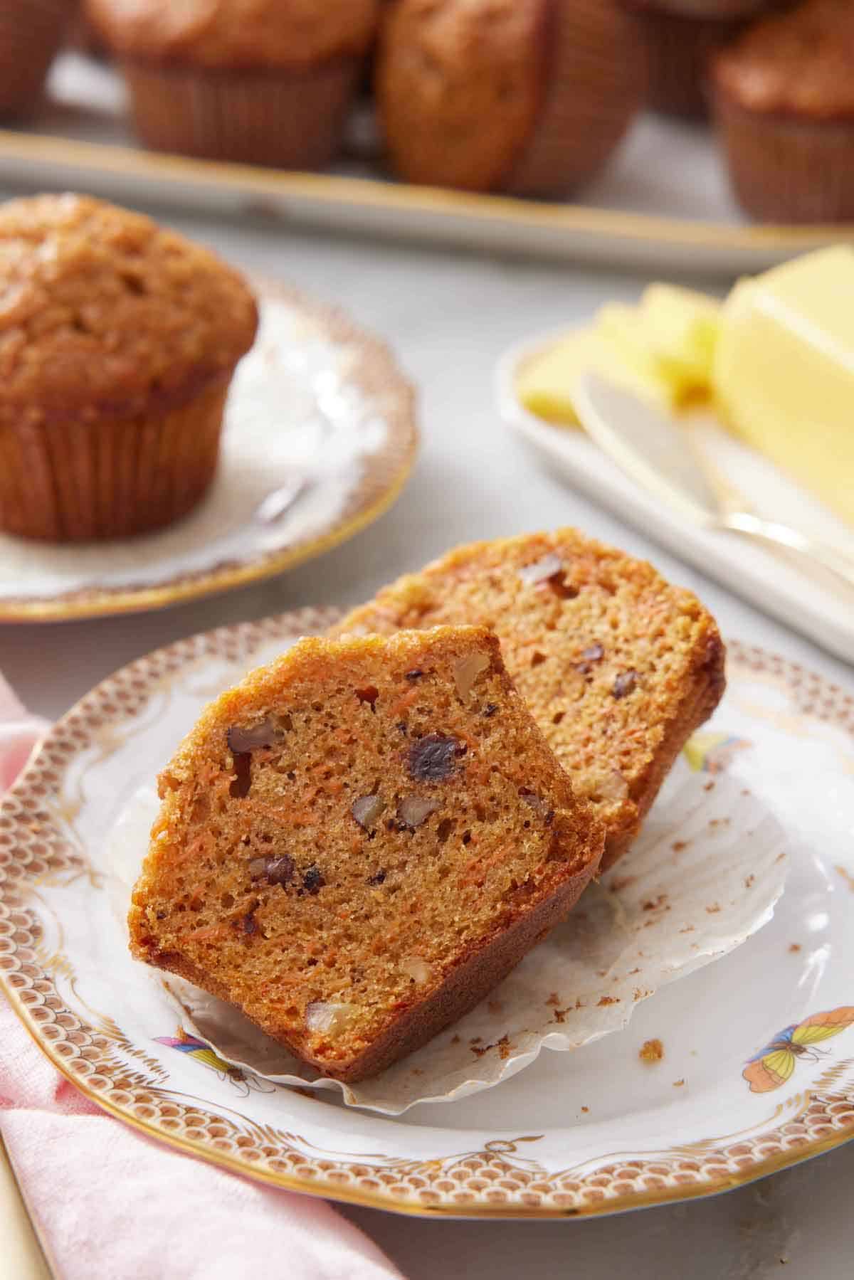 A plate with a carrot muffin cut in half on a plate. More muffins in the background with butter on a dish.