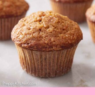 Pinterest graphic of a carrot muffin on a marble surface with more in the background.