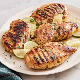 A platter with four cilantro lime chicken garnished with chopped cilantro and cut limes. A napkin on the side.
