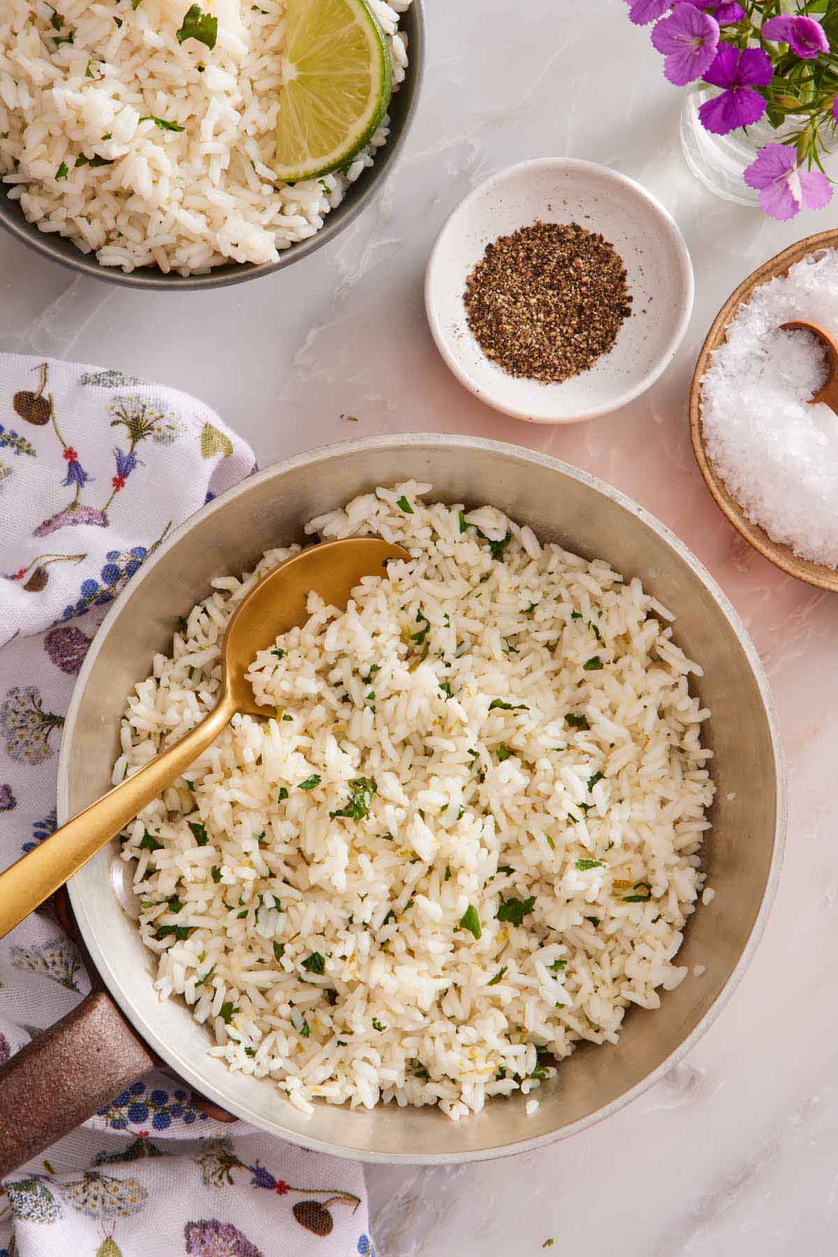 Overhead view of cilantro lime rice in a small pot with a spoon inside. A plate of salt, pepper, and another bowl of rice in the background.