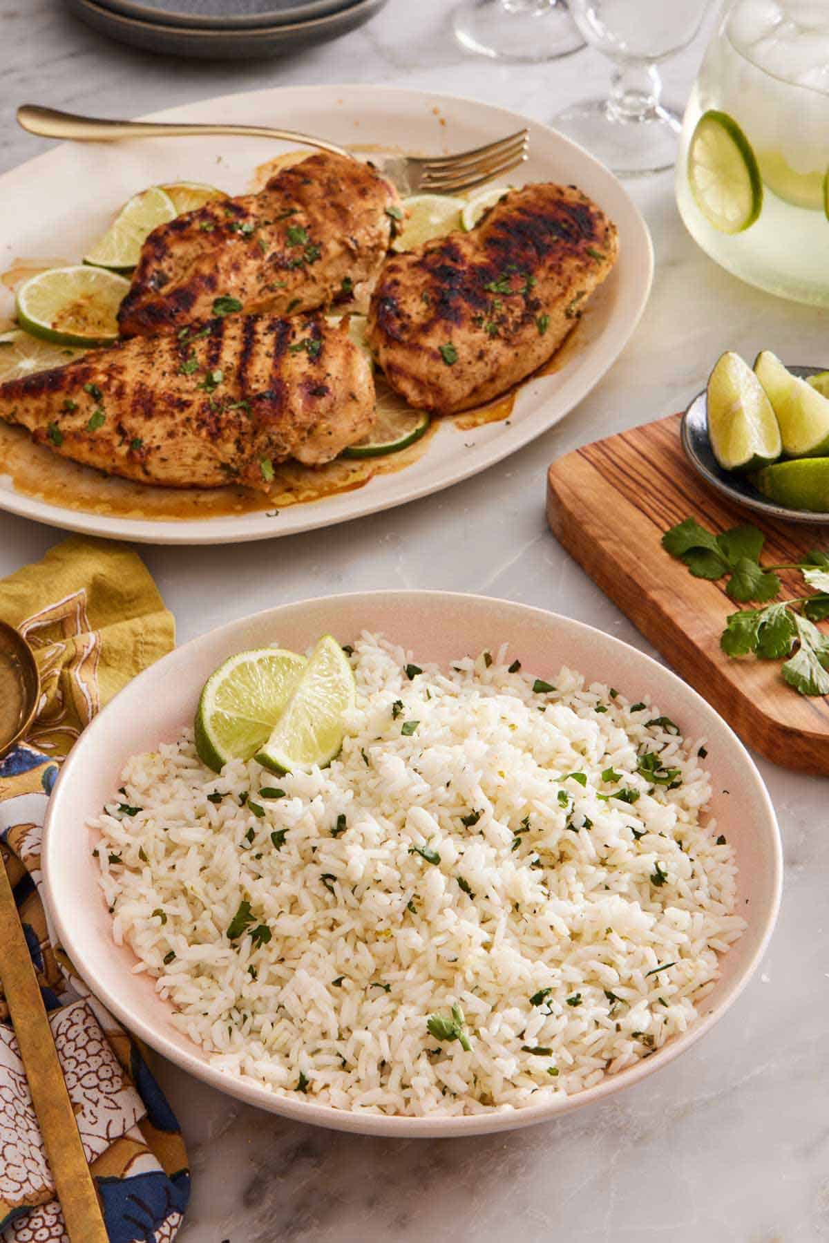 A bowl of cilantro lime rice with grilled chicken in the background. Cut limes and cilantro on the side.