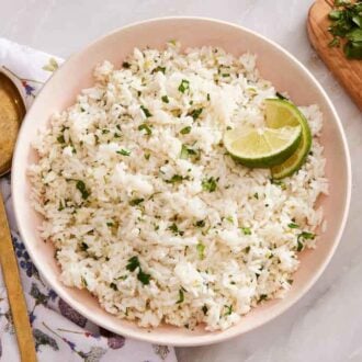 Overhead view of a plate of cilantro lime rice cut limes. A serving spoon on the side along with some cut limes and cilantro.