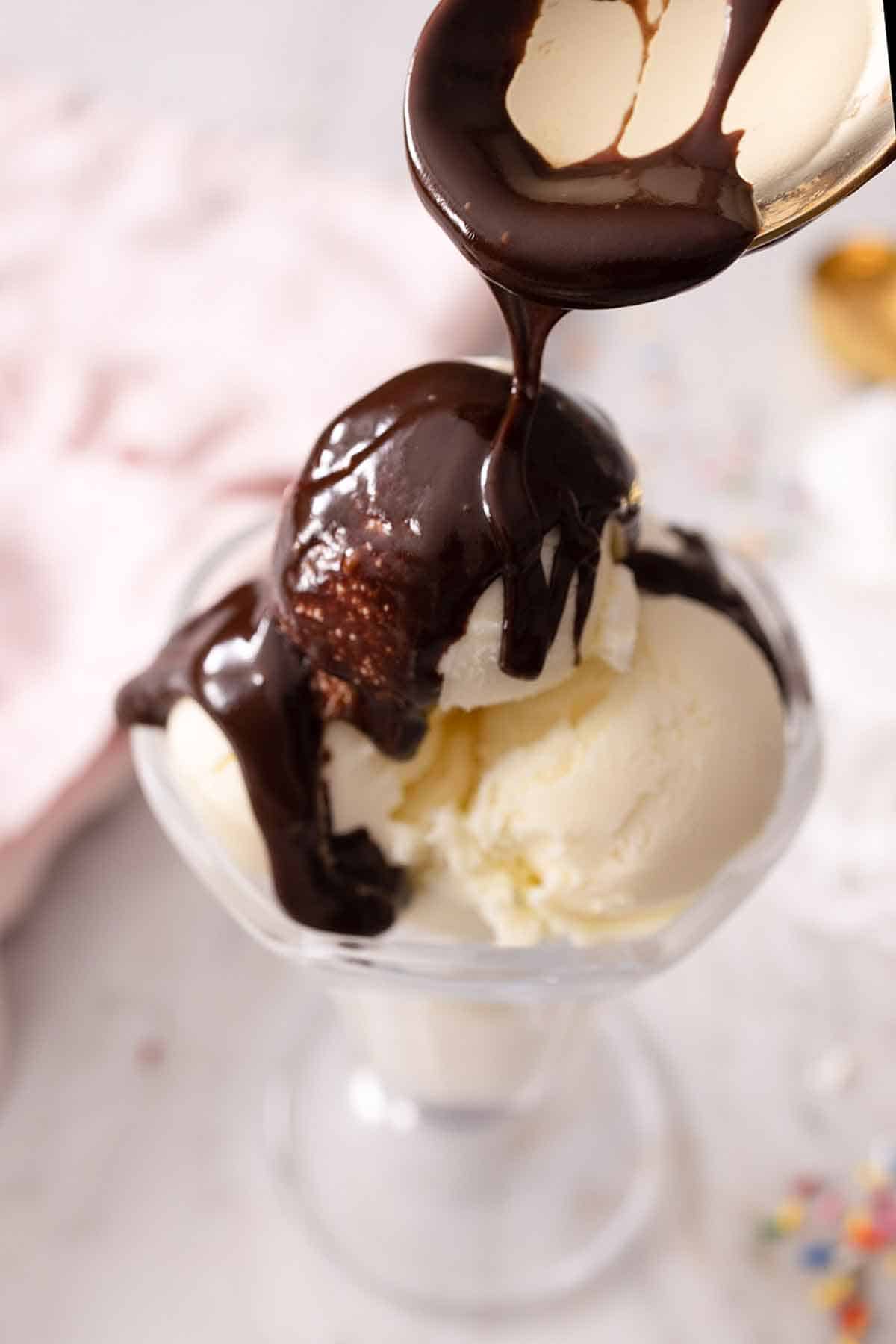 Hot fudge sauce spooned over a bowl of vanilla ice cream.