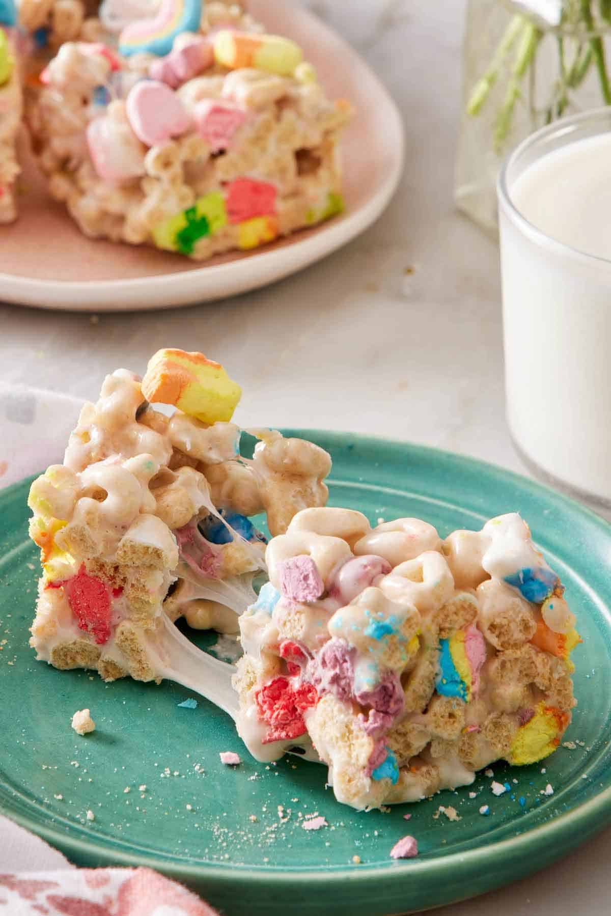 A plate with a Lucky Charms treat torn opened, showing the melty marshmallows. A glass of milk and more Lucky Charms treats in the background.
