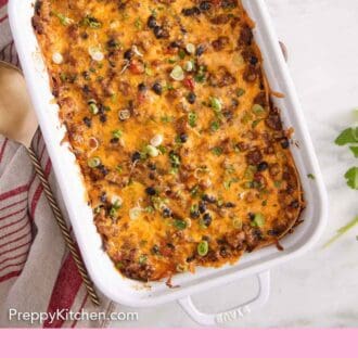 Pinterest graphic of a baking dish of Mexican lasagna with green onion garnish.