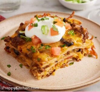 Pinterest graphic of a plate with a serving of Mexican lasagna with a dollop of sour cream on top with chopped tomatoes and green onions.