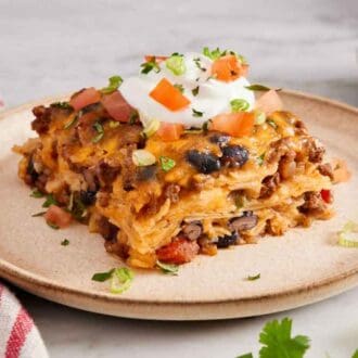 a plate with a serving of Mexican lasagna with sour cream, tomatoes, and green onions on top.