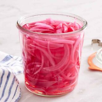 A jar of pickled red onions with a napkin and lid off to the side.