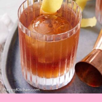 Pinterest graphic of a glass of Vieux Carré with a round ice cube and a lemon peel garnish. A jigger beside it.