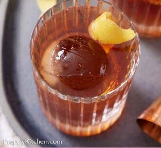 Pinterest graphic of a slightly overhead view of a glass of Vieux Carré with one ice cube with a lemon peel garnish. More lemon peels in the background.
