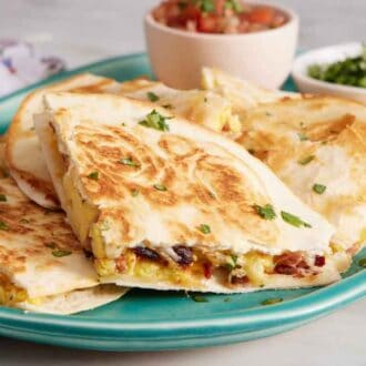 A platter of breakfast quesadillas and a bowl of pico de gallo and chopped cilantro.