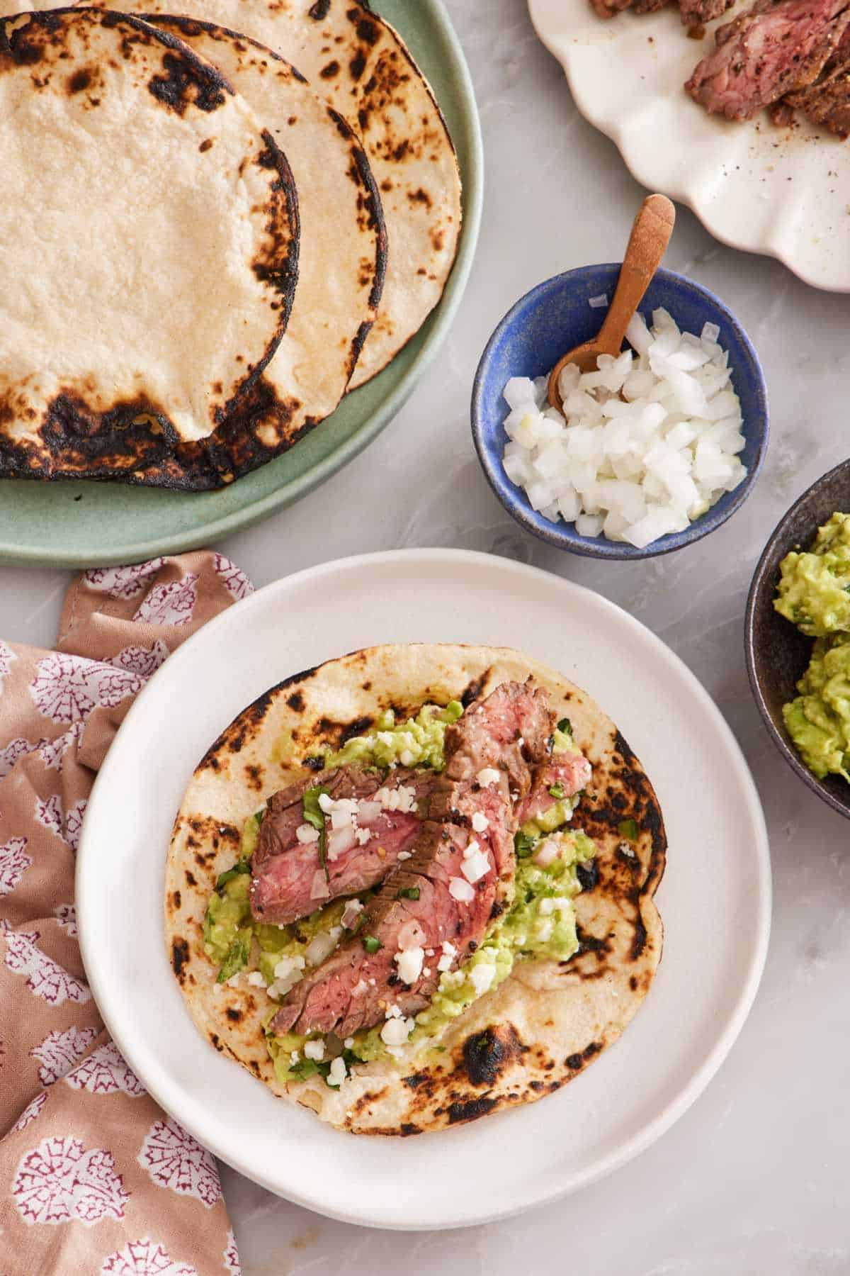 Overhead view of a carne asada taco with grilled corn tortillas, chopped onions, and guacamole on the side.