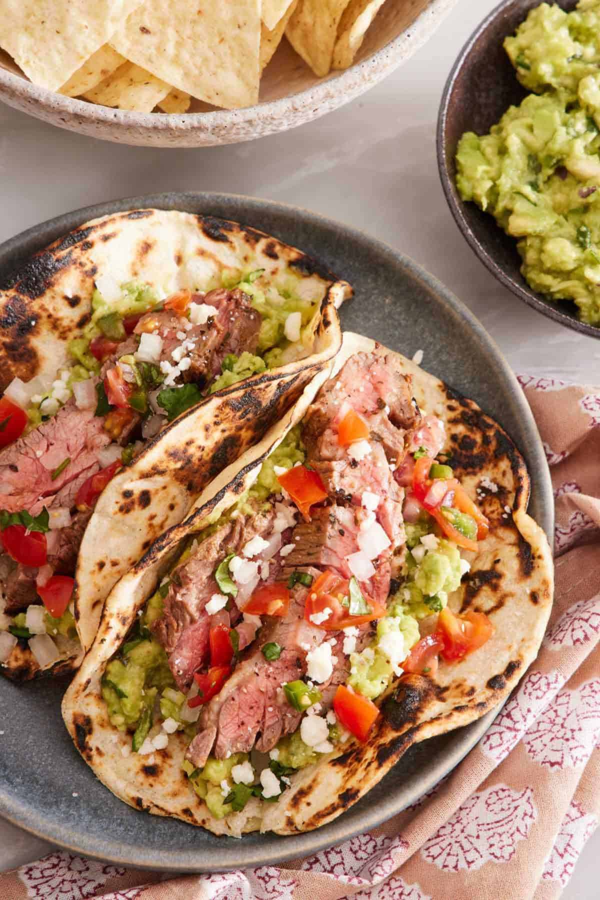 Two carne asada tacos garnished with chopped cilantro, crumbled cheese, and pico de gallo.