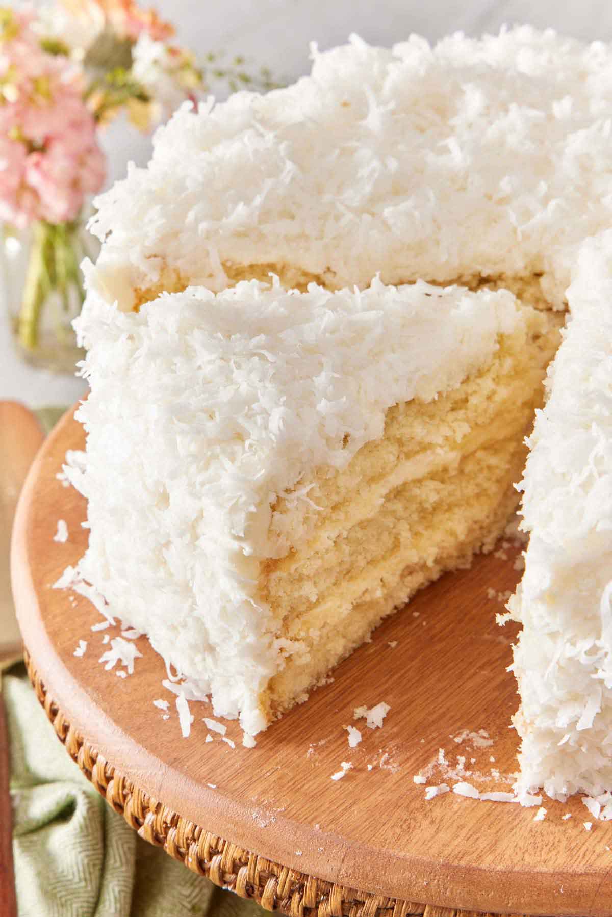 A slice of coconut cake cut from the cake on a cake stand and slightly pulled forward.