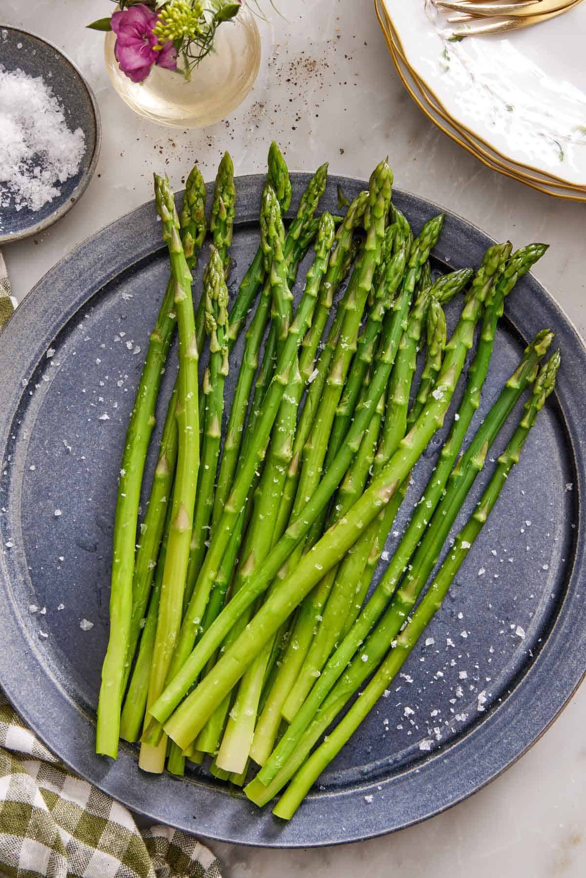 An overhead view of a large plate of blanched asparagus topped with flaky salt.