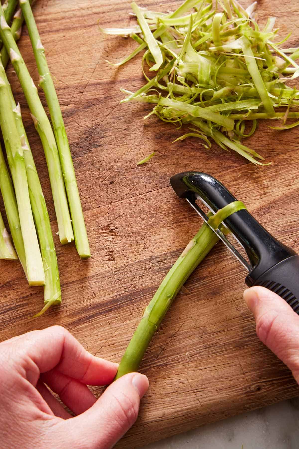 A vegetable peeler peeling the woody ends of an asparagus.