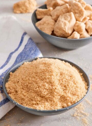 A bowl of softened brown sugar with a bowl of hardened brown sugar in the background.