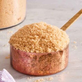 A measuring cup of softened brown sugar. A jar of brown sugar in the background.