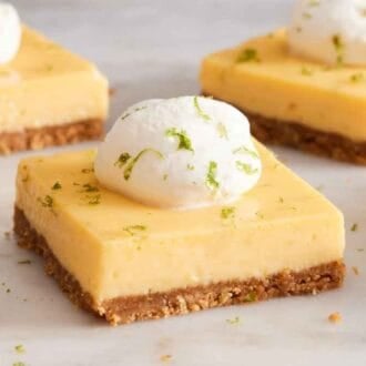 Multiple key lime pie bars on a marble surface, all topped with whipped cream and lime zest.