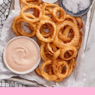 Pinterest graphic of a lined baking sheet with onion rings, bowl of salt, pepper, and dipping sauce.