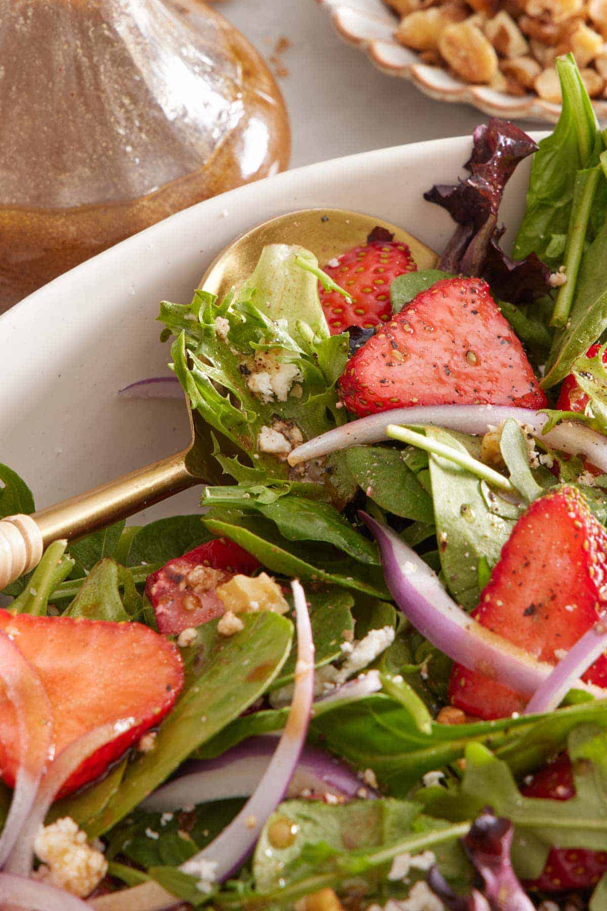 A close up view of a spoon tucked into a bowl of strawberry salad.