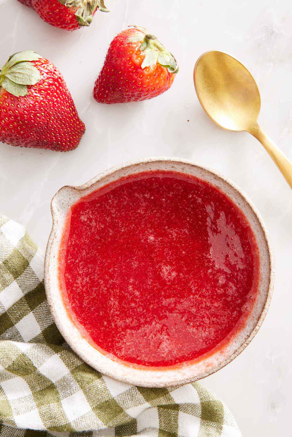 Overhead view of a bowl with a lip of strawberry syrup. A strawberry, napkin, and spoon on the side.