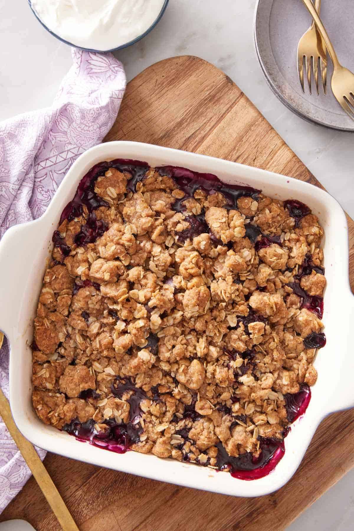 Triple berry crisp in a white baking dish placed on a wooden board.