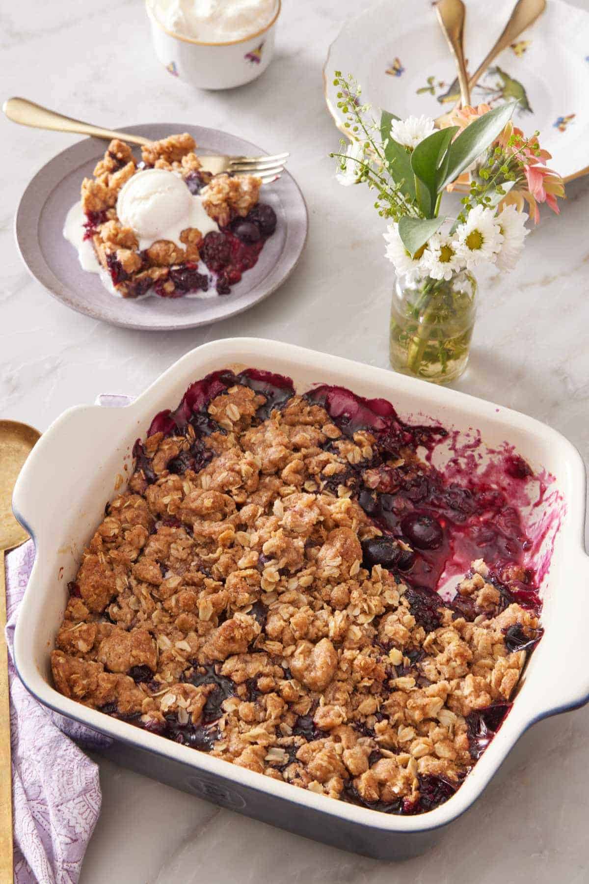 Fruit crisp in a baking dish with some scooped out and served on a small plate in the background.