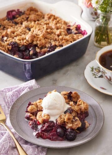 Berry crisp topped with ice cream with coffee and more crisp in the background.