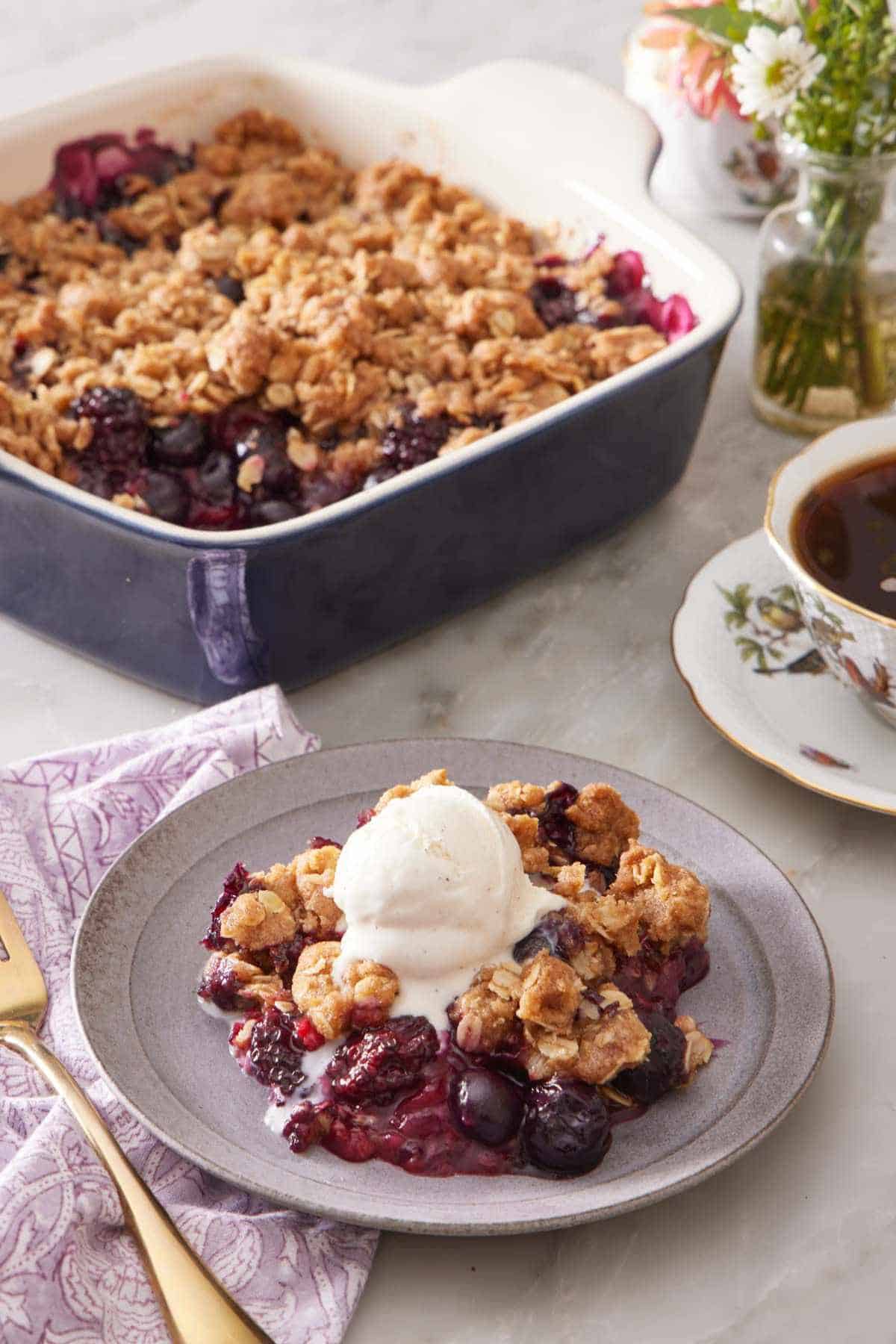 Berry crisp topped with ice cream with coffee and more crisp in the background.