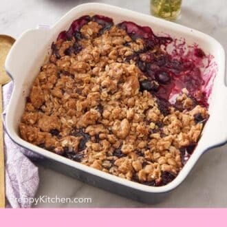 Pinterest graphic showing mixed berry crisp in a baking dish with some scooped out.